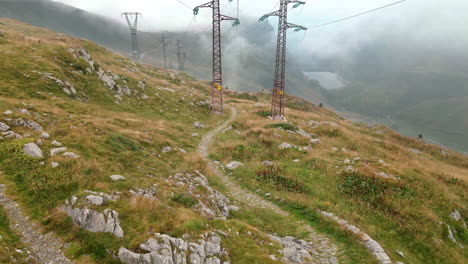 Cinematic-View-Of-The-High-Voltage-Pylons-Above-The-Meadows-Of-The-Alpine-Mountain-In-Passo-San-Marco,-Northern-Italy---Aerial-drone-shot