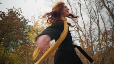 joyful woman with yellow beret and sunglasses playfully spins around, her yellow muffler swaying in the breeze, as she enjoys a vibrant autumn day in the forest