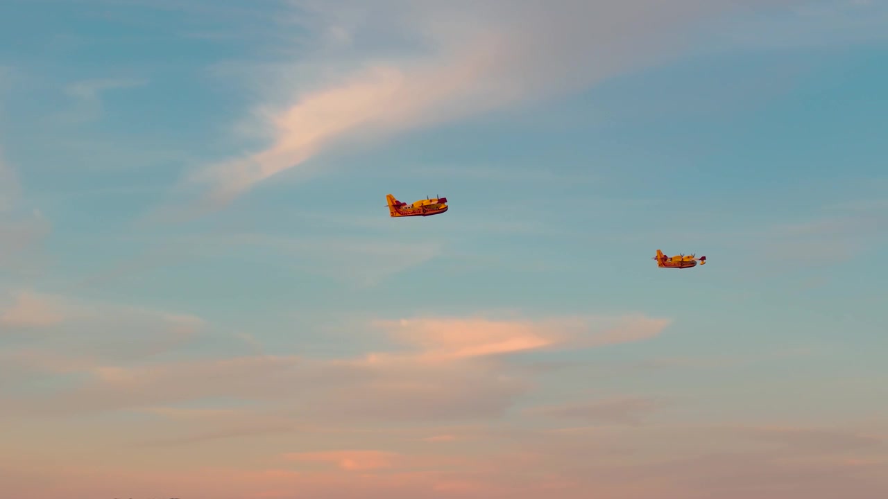En horisontal udsigt ved dagens slutning over en sø, med to Canadair-fly, der var kommet for at hente vand og nu er på vej tilbage for at bekæmpe en brand
