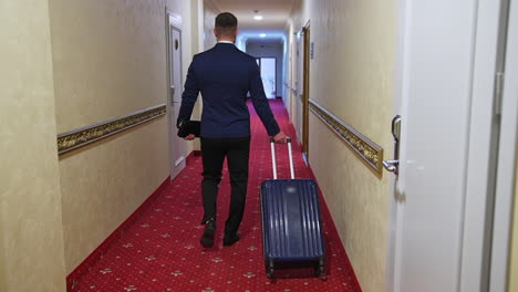 a man with a suitcase is walking down a hotel hallway. dark red carpet in a hotel hall. view from the back on a businessman in a trip.