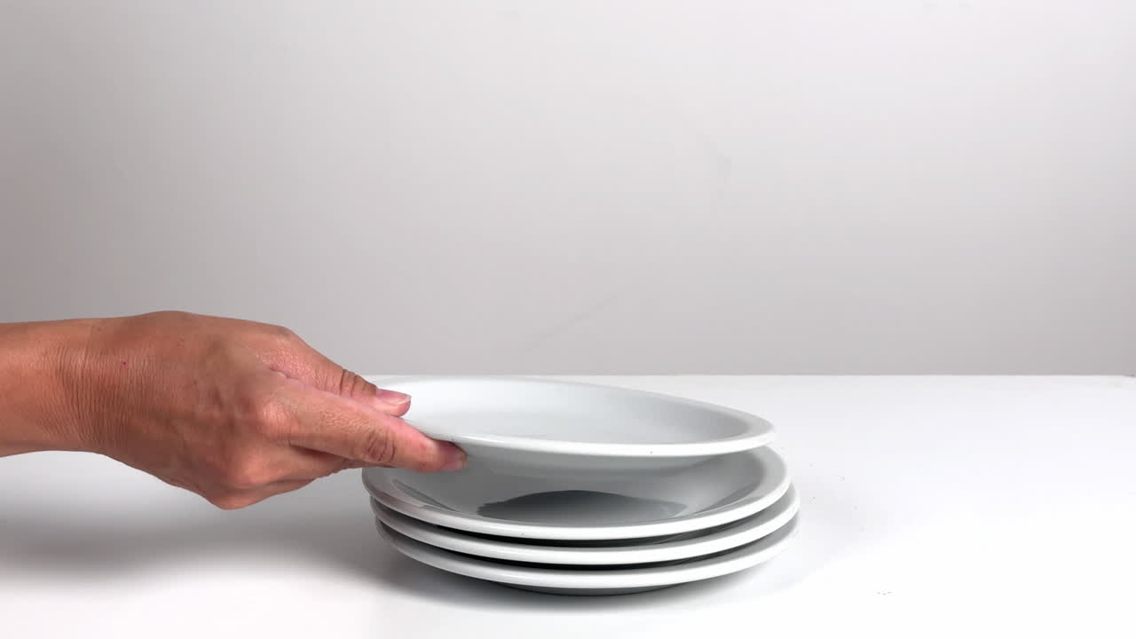 Hand Stacking Clean White Plates on a White Surface