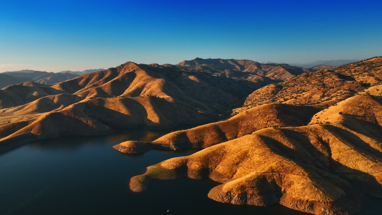 Slopes of bare brown mountains descending into the lake. Setting sun lighting the smooth rocks. California desert top view.