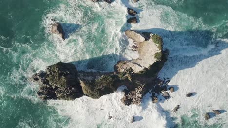 ascending top down drone shot of waves crashing on island in ocean