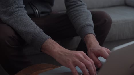 cerca de las manos del hombre escribiendo en una computadora portátil en su casa sentado en el sofá
