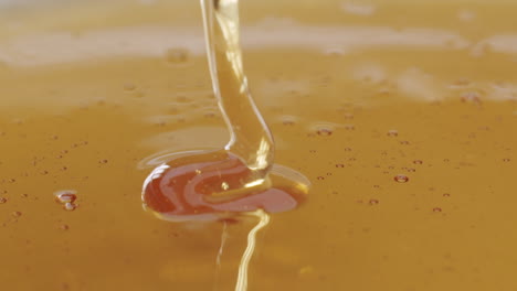 macro close up shot of honey getting poured into honey on a plane surface