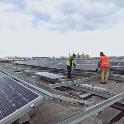 engineers carry solar panel on a solar farm. two workers installing blue sunny battery on a metal basis on a rooftop. clean environmental energy from the sun.