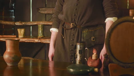 sirviente medieval se encuentra en el mostrador en la taberna. barman enano con bolso en el cinturón listo para vender bebidas y bienes en la casa pública. personaje de fantasía npc