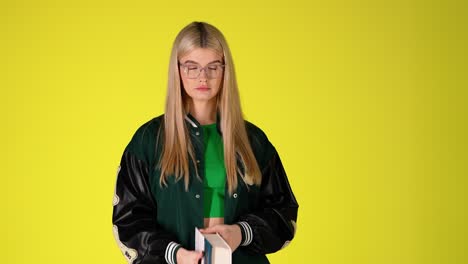 estudiante rubia bonita da la vuelta a las páginas de un libro y mirando a la cámara, colorido estudio disparado