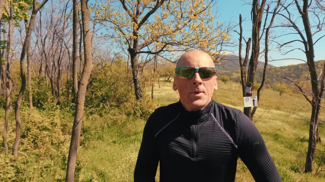 Homem maduro ativo na casa dos 50 anos correndo numa trilha através de um campo e floresta cénicos num dia ensolarado de primavera. Estilo de vida sénior saudável, correndo e exercitando-se ao ar livre. Filmagens 4k de alta qualidade