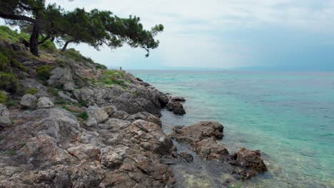 Vista-Aérea-De-La-Línea-Costera-Rocosa-Cerca-De-La-Playa-De-Glifoneri,-Con-Agua-Turquesa-Y-Follaje-Verde-Exuberante,-Isla-De-Thassos,-Grecia,-Europa