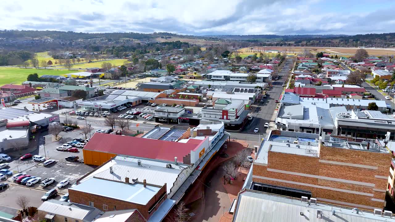 Drone camera glides above a small-town main street in Armidale, NSW, revealing rooftops, parked cars, and surrounding countryside under bright daylight