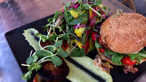 bright vibrant side salad and gourmet hamburger on a black plate and dressing