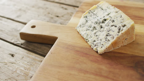 video of wedge of blue cheese on chopping board, on rustic wooden table