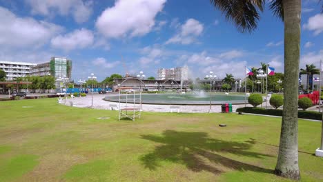 a drone shot moving towards the fountain of bacolod city's new government center. it is a bright and sunny day. there are palm trees around too.