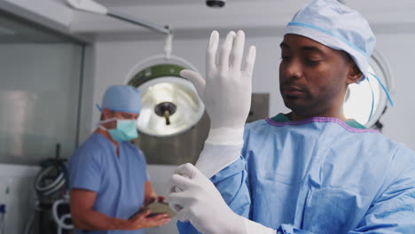 portrait of male surgeon wearing scrubs putting on latex gloves in hospital operating theater