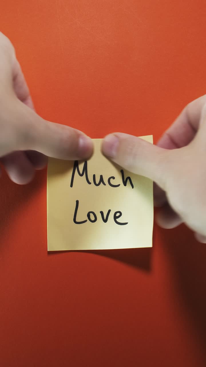 Much Love message on yellow sticky note against bold orange wall, symbolizing warmth and affection