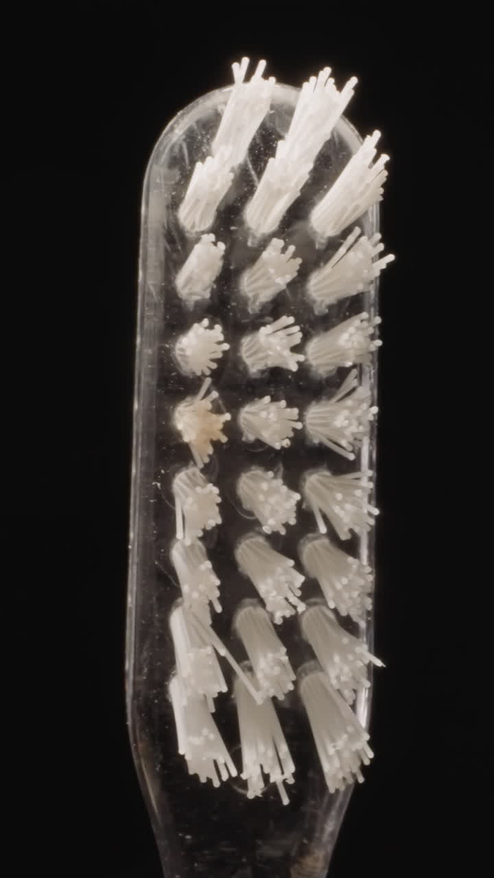 Transparent plastic toothbrush with hard white bristles turning on black background. Small brush designed for professional oral hygiene macro