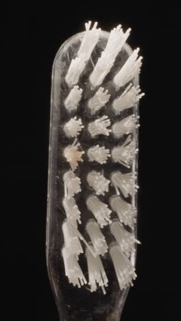transparent plastic toothbrush with hard white bristles turning on black background. small brush designed for professional oral hygiene macro