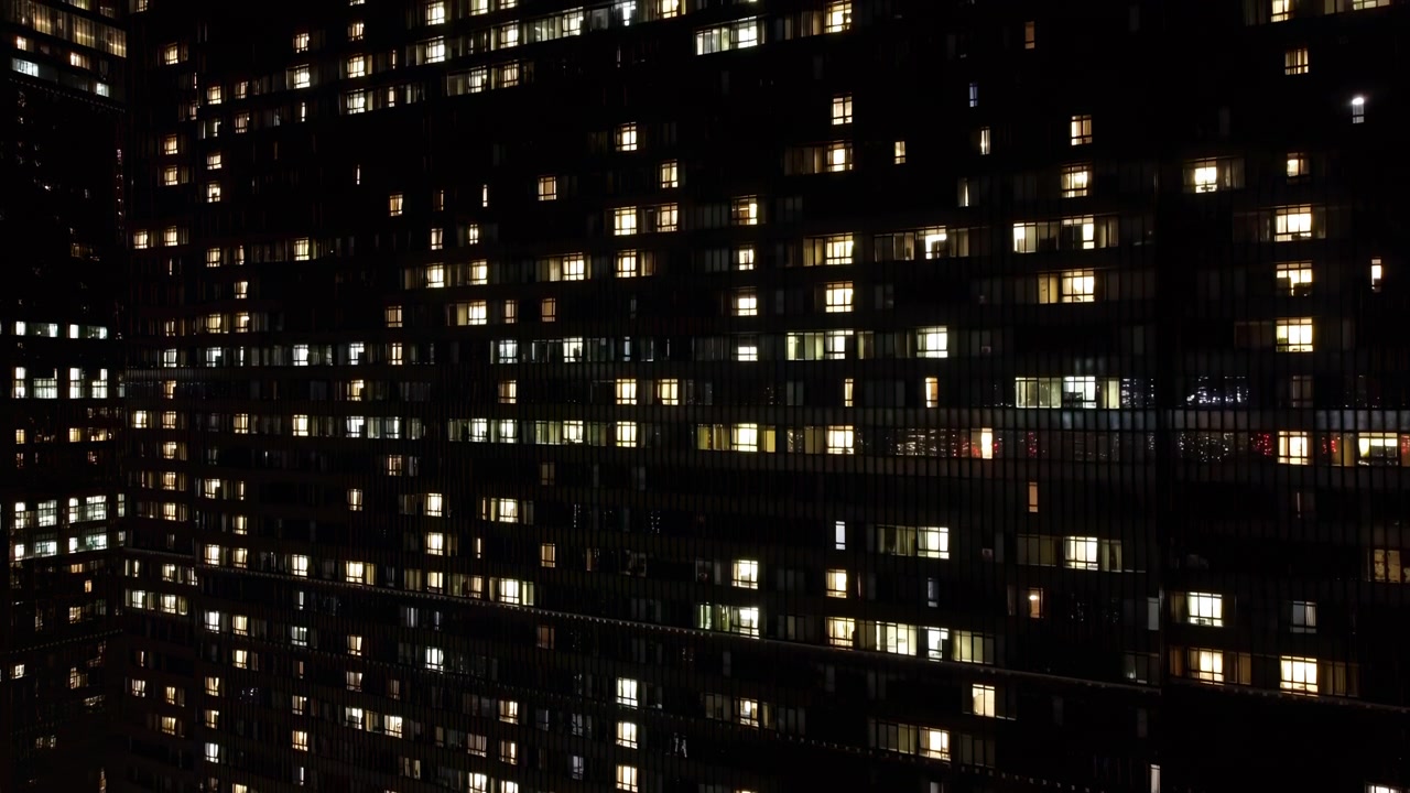 Finestre della città notturna illuminate, facciata di un condominio denso con finestre illuminate che formano un mosaico a griglia.