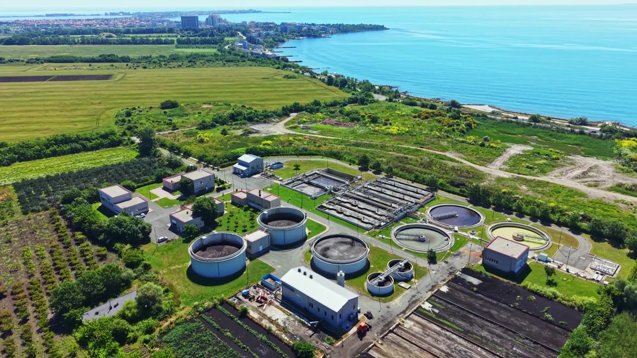 Water treatment facility near a lake with green fields and urban landscape in the distance