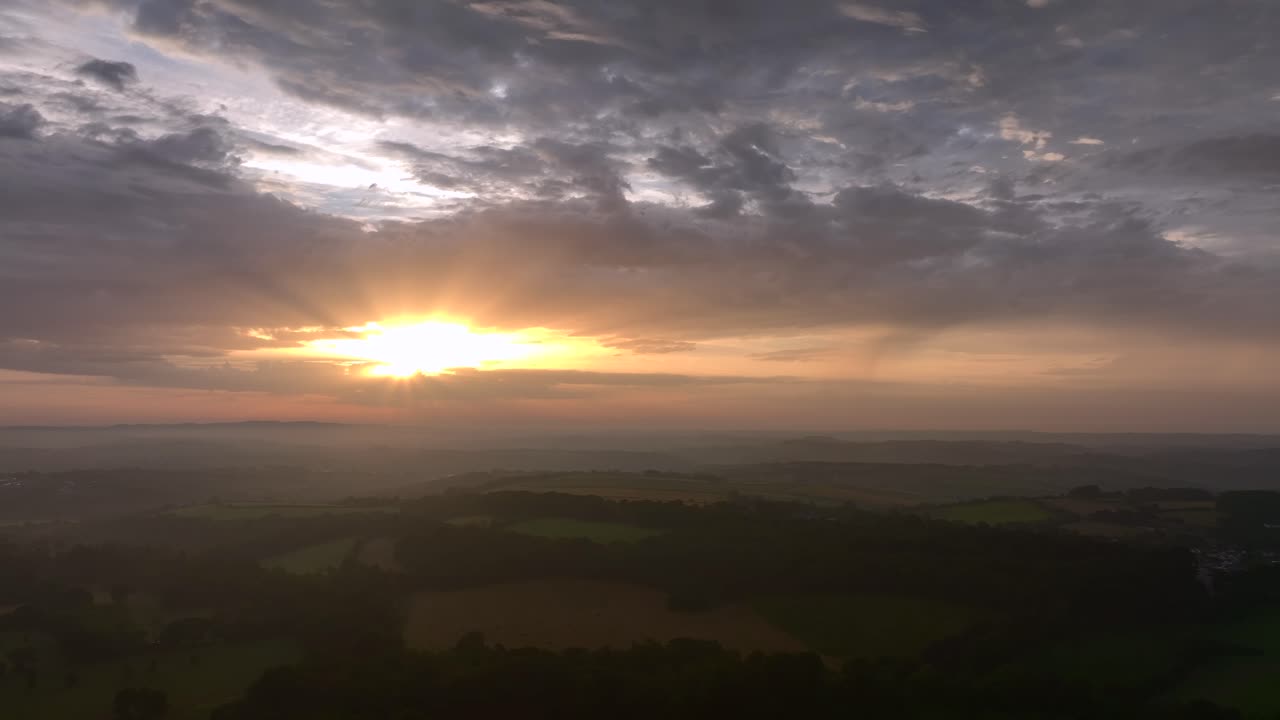 Patchwork misted fields, woodland and hedgerows at dawn in South West England. Camera reverses over landscape. Summer. Cornwall, UK.