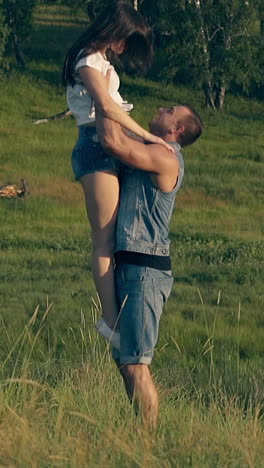 young brunette woman runs on green meadow to handsome man and jumps into arms against trees slow motion