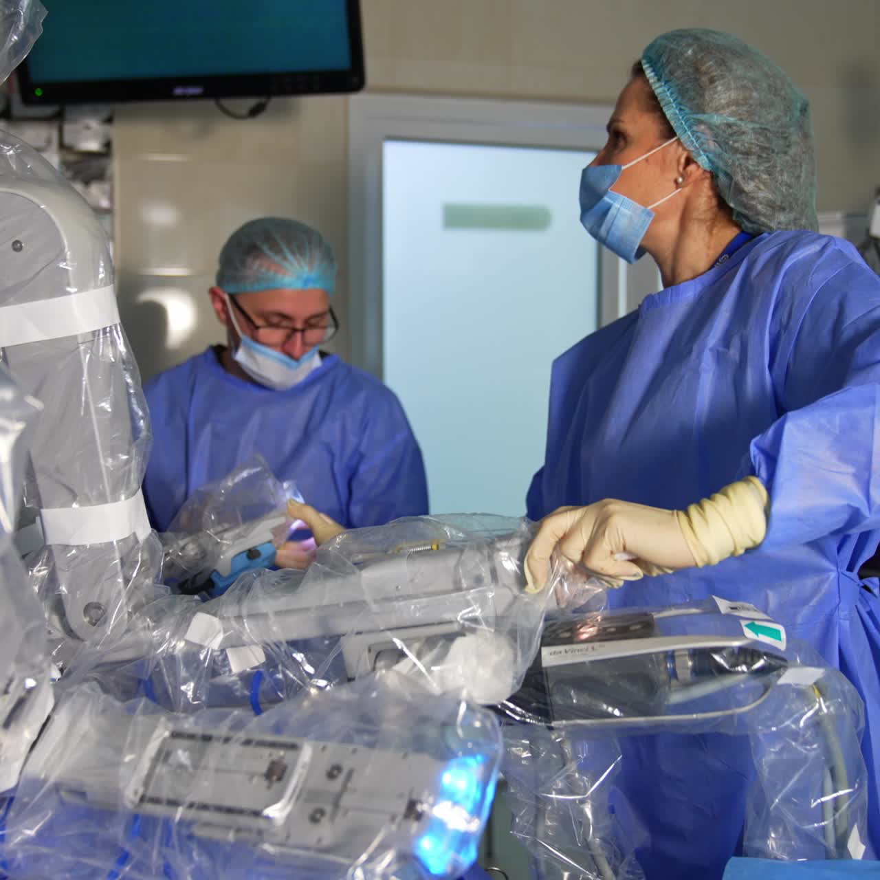 Female medic standing in the operative field of Da Vinci robot holding by the robotic arm. Doctor moves the arm looking at the screen and takes another one