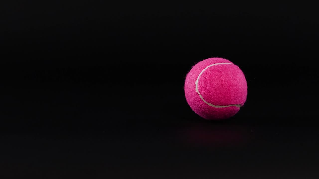 A bright pink tennis ball falls and bounces repeatedly against a dark, minimalist studio background