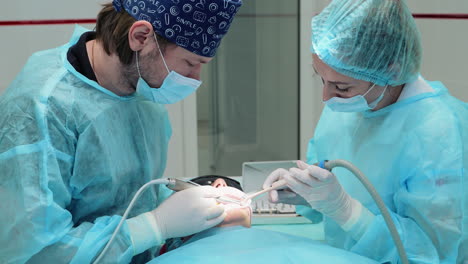 vinnytsia, ukraine - may 20, 2023: male dentist with assistant uses drill to treat caries in teeth of female patient sitting in chair. dental clinic helps patients