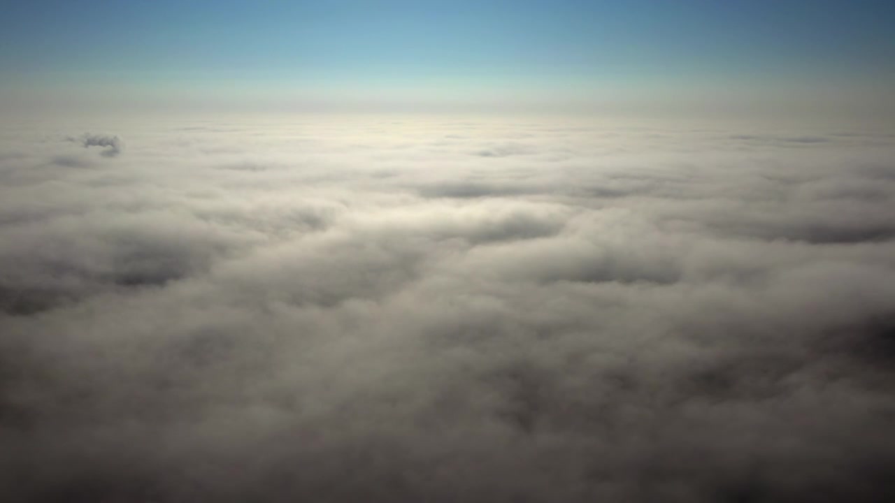 Aerial from an airplane view above a soft cloud layer stretching to horizon Cinematic with blue sky horizon and peaceful atmospheric travel mood altitude atmosphere abstract sky landscape