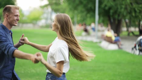 the guy dances with the girl in the park. young people hold hands and have fun. happiness