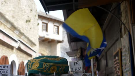 Small-flag-of-Bosnia-and-Herzegovina-fluttering-in-the-wind-beside-a-traditional-skullcap-or-taqiyah