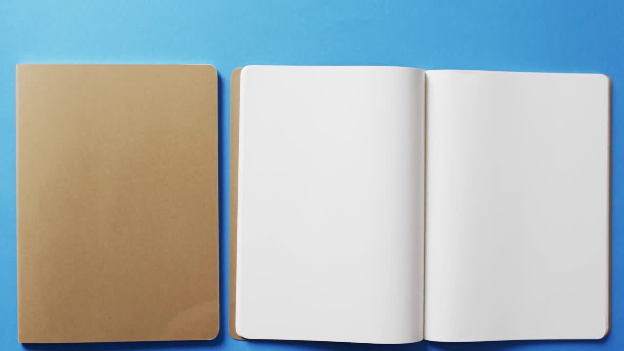 Close up of open blank book and brown notebook with copy space on blue background in slow motion