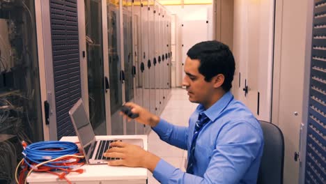 Technician-talking-on-mobile-phone-in-while-working-on-laptop