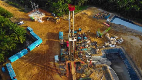 Cinematic-4K-Drone-Footage-of-Onshore-Drilling-Rig-equipment-structure-for-oil-exploration-and-exploitation-in-the-middle-of-jungle-surrounded-by-palm-oil-trees-during-sunset-and-high-oil-price