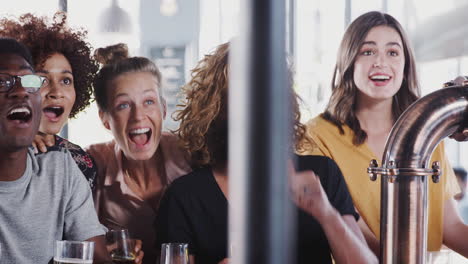 Grupo-De-Amigos-Y-Amigas-Celebrando-Mientras-Ven-El-Juego-En-La-Pantalla-En-El-Bar-Deportivo