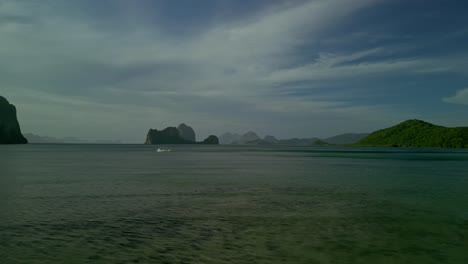 Boat-at-sea-by-green-hilly-islands-in-Philippines,-wide-forward-aerial