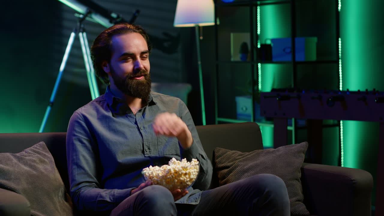 hombre riendo de programas divertidos en la televisión, comiendo bocadillos, sentado en el sofá