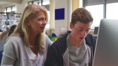 teacher with male student working on computer in college library