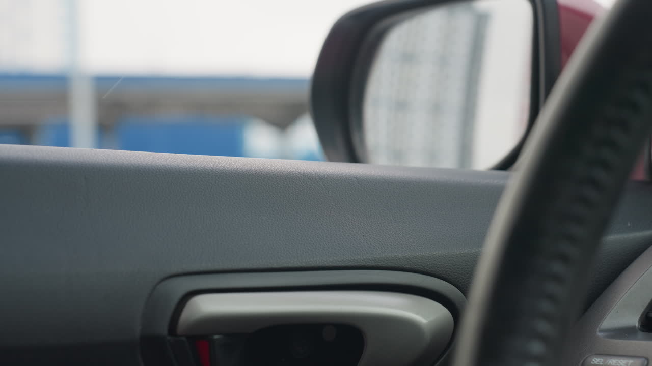 car window slides down as snowflakes drift past exterior revealing blurred industrial buildings outside view through glass with streaks cold overcast atmosphere visible steering wheel