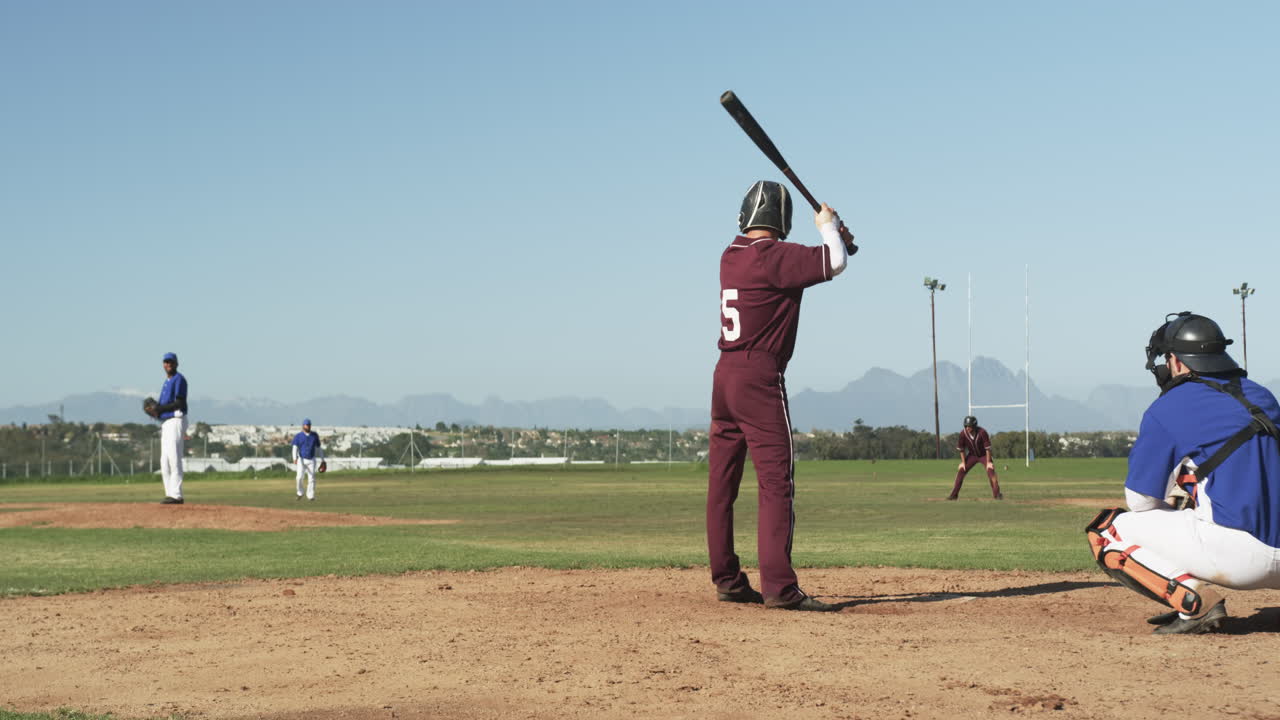 Playing baseball, batter in maroon uniform preparing to hit pitched ball