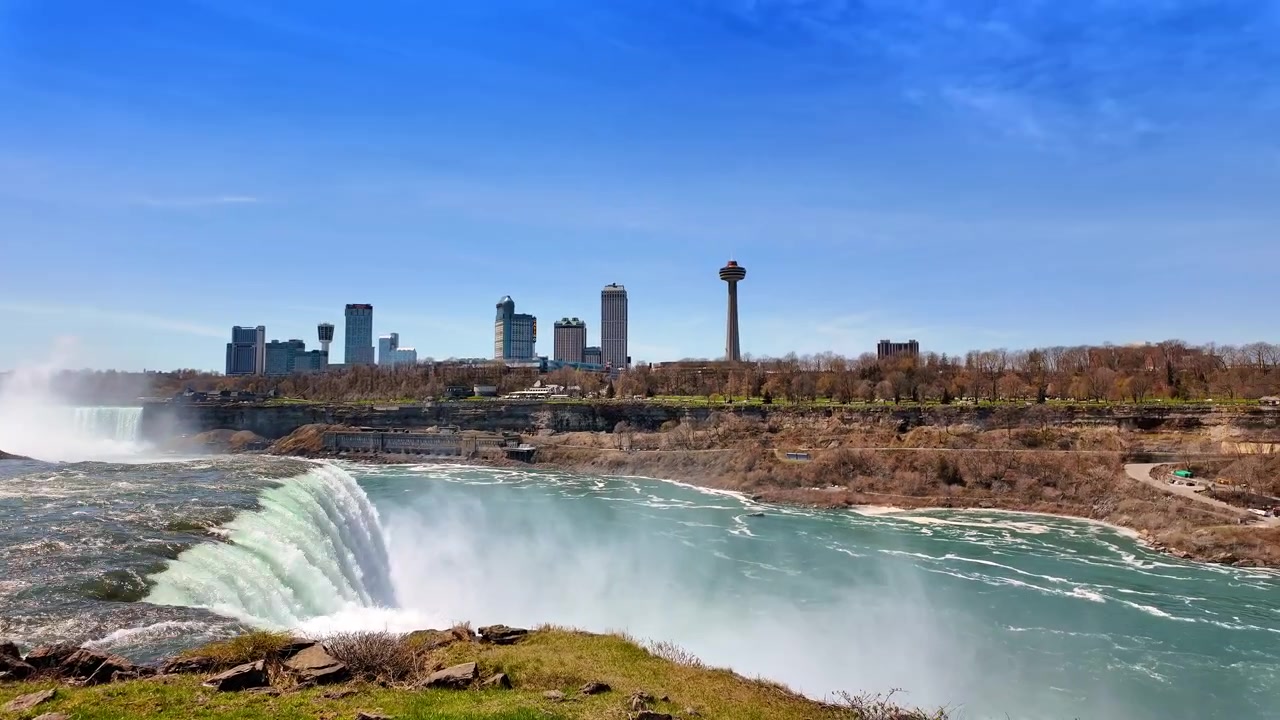 Vista de las Cataratas del Niágara con el horizonte de la ciudad y la torre de observación durante el día. El agua fluye sobre las Cataratas del Niágara.