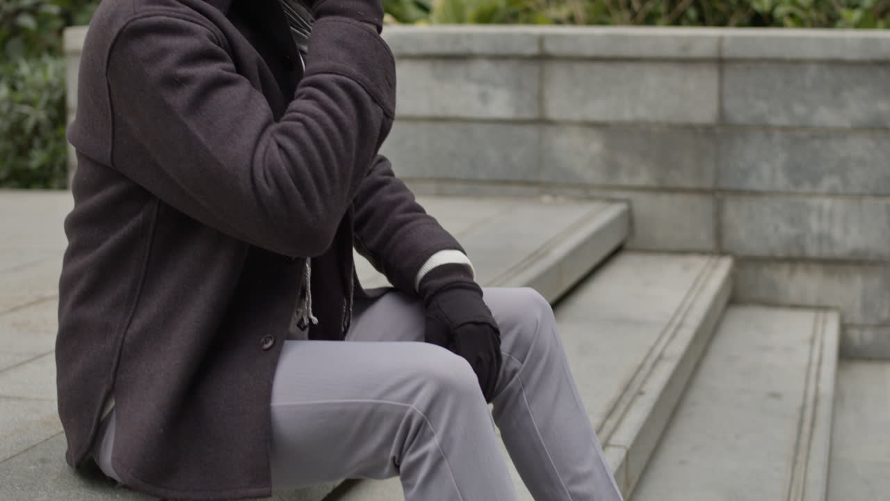 인과적 인 가을 옷을 입은 남자가 비즈니스 사무실 건물의 콘크리트 계단에 앉아 적극적으로 전화로 이야기합니다.