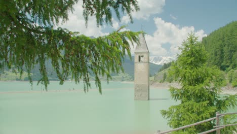 Tiro-Medio,-Rama-De-árbol-Que-Sopla-En-El-Viento-En-Italia,-Kirchturm-Von-Altgraun-En-El-Lago-De-Reschensee-En-El-Fondo