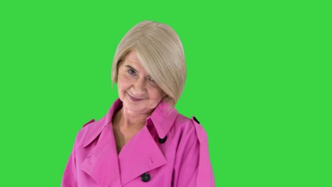 trendy beautiful senior woman in a pink coat walks in and showing her outfit to camera on a green screen, chroma key