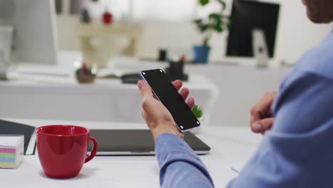 Caucasian-businessman-having-video-call-using-smartphone-at-desk-in-office