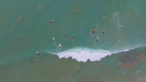 Surfers-dive-and-paddle-under-breaking-wave-on-colorful-board,-aerial-top-down