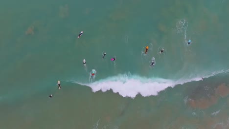 surfers dive and paddle under breaking wave on colorful board, aerial top down