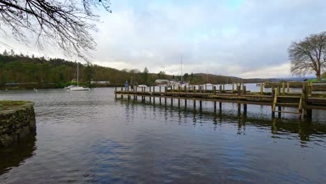 lake windermere in the english lake district, with its iconic wooden jetty, historic stone-built buildings, and moody grey skies