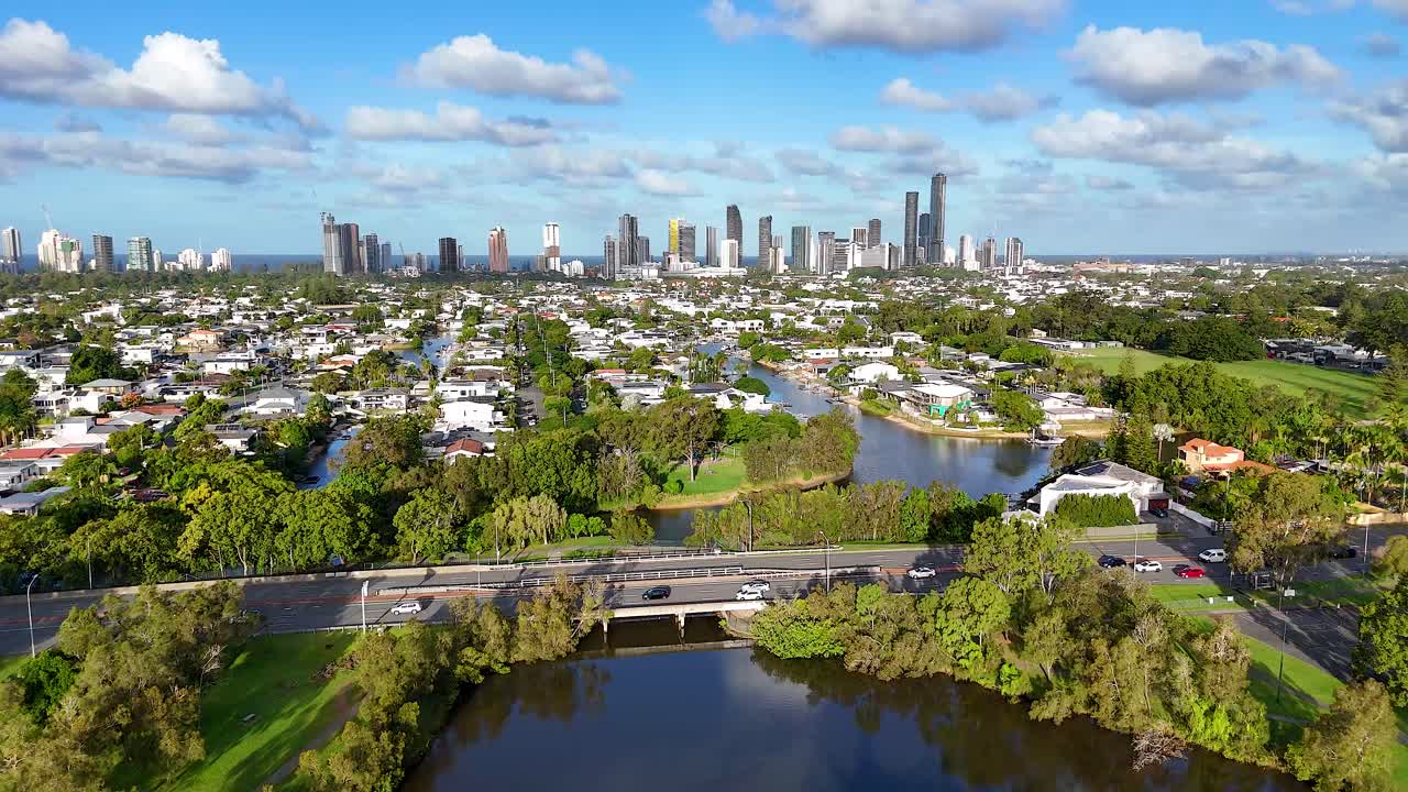 Aerial footage of Gold Coast, Australia, showcasing city skyline, lush greenery, and a winding river under clear blue skies